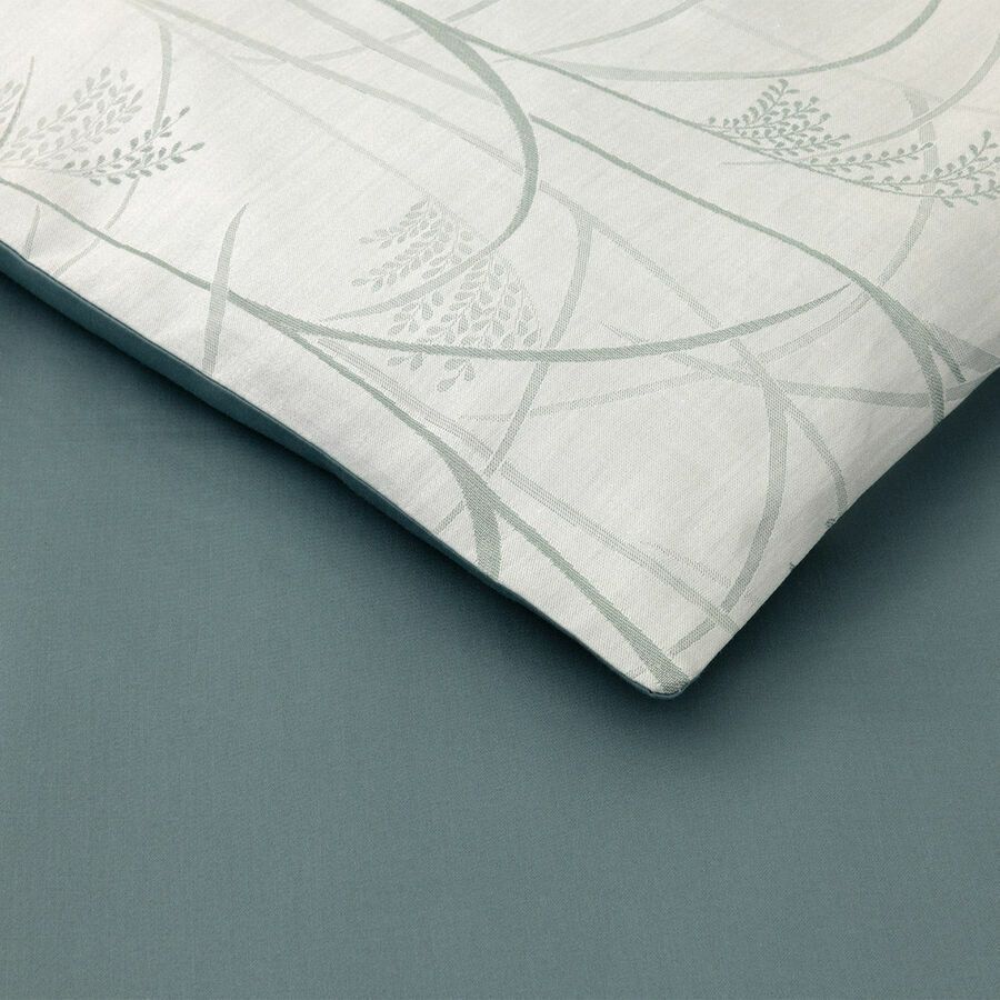 Coussin blanc à motif floral vert pâle sur fond bleu.