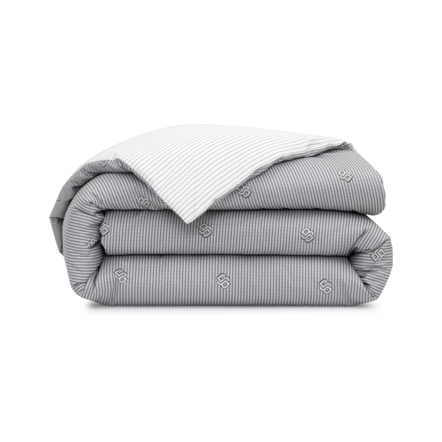 Une couette pliée, gris clair, à fines rayures blanches et ornée de petits motifs circulaires brodés.
