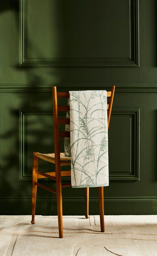 Chaise en bois avec une serviette à motifs drapée contre un mur lambrissé vert foncé.