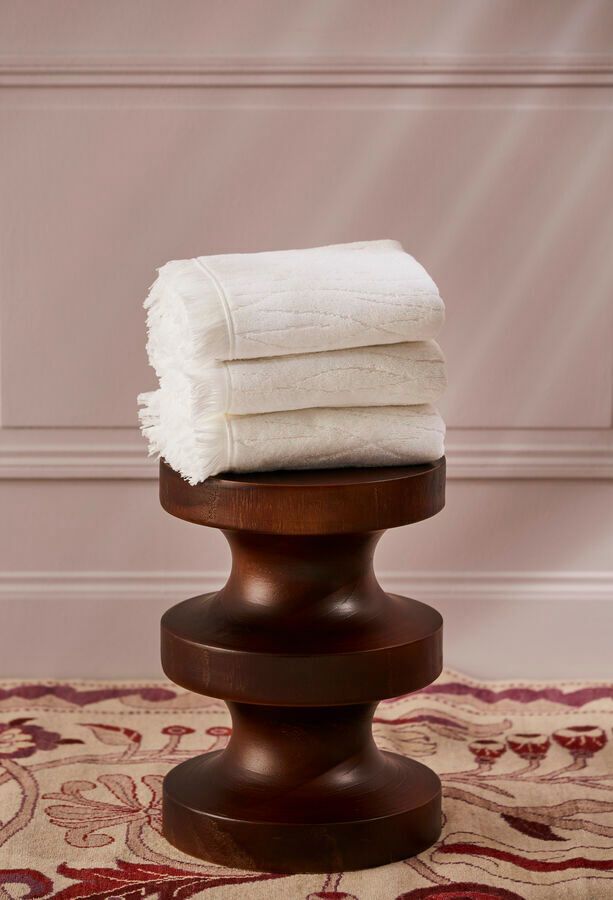 Pile de serviettes blanches sur un tabouret en bois foncé, devant un mur rose clair.