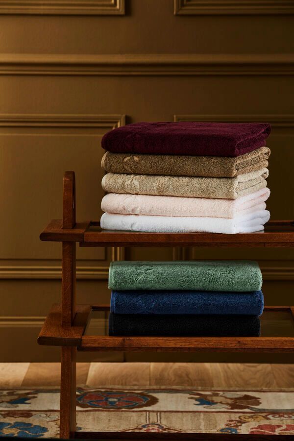 Pile de serviettes colorées pliées sur une étagère en bois ; un mur jaune moutarde foncé en arrière-plan.