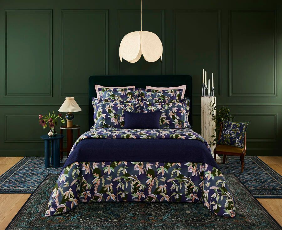 Chambre avec linge de lit bleu marine à motifs floraux, murs vert foncé, tapis et suspension lumineuse.