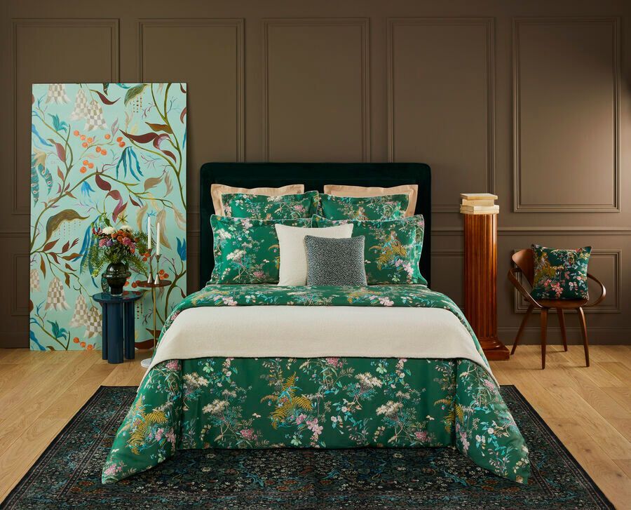 Chambre à coucher avec linge de lit à motifs floraux, œuvres d'art et meubles dans les tons de vert, de bleu et de marron.