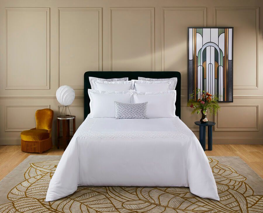 Des draps blancs sur un lit dans une chambre beige avec un tapis et des œuvres d'art dorés.