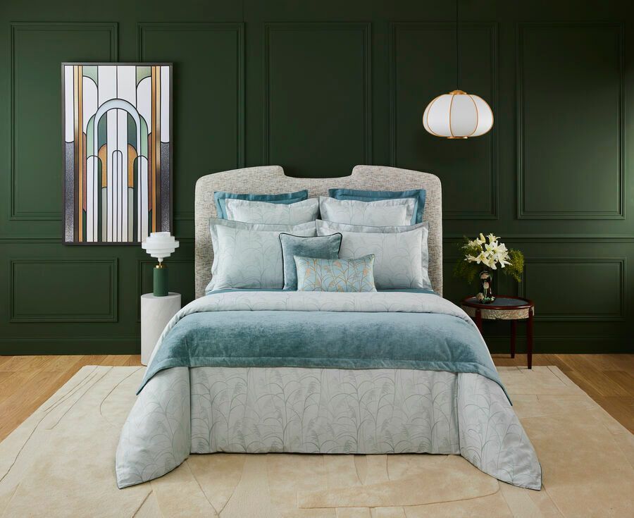 Chambre avec un couvre-lit turquoise, une couette à motifs et un mur vert orné d'une peinture abstraite.
