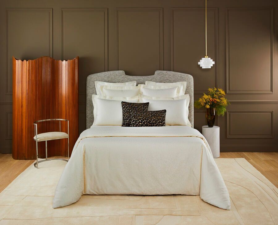 Chambre avec linge de lit couleur crème, tête de lit texturée, murs marron et mobilier moderne.