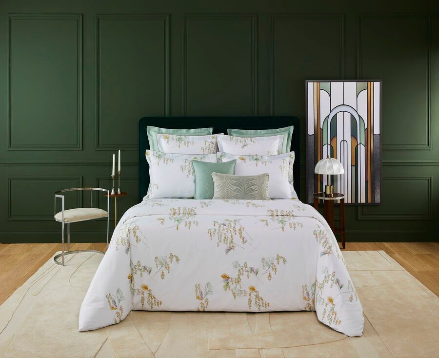 Lit avec linge de lit à motifs floraux contre un mur lambrissé vert ; chaise, tapis et œuvre d'art.