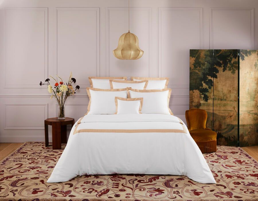 Chambre avec literie blanche, boiseries beiges, tapis, luminaires dorés et décorations florales.