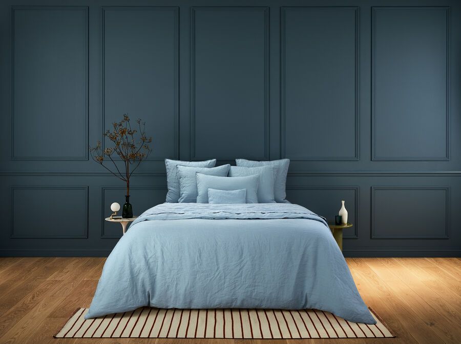 Un lit avec une couette et des oreillers bleus dans une chambre aux murs bleu foncé.