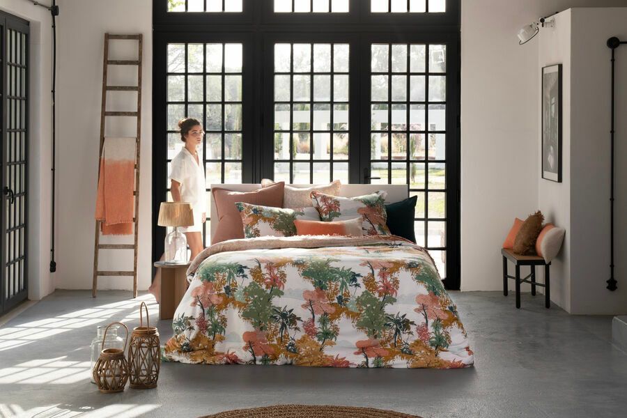 Une femme se tient debout à côté d'un lit dans une chambre.