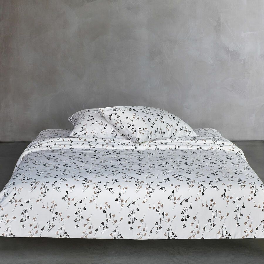 Un lit bas avec une couette blanche et deux oreillers ornés d'un délicat motif floral foncé sur un mur gris.