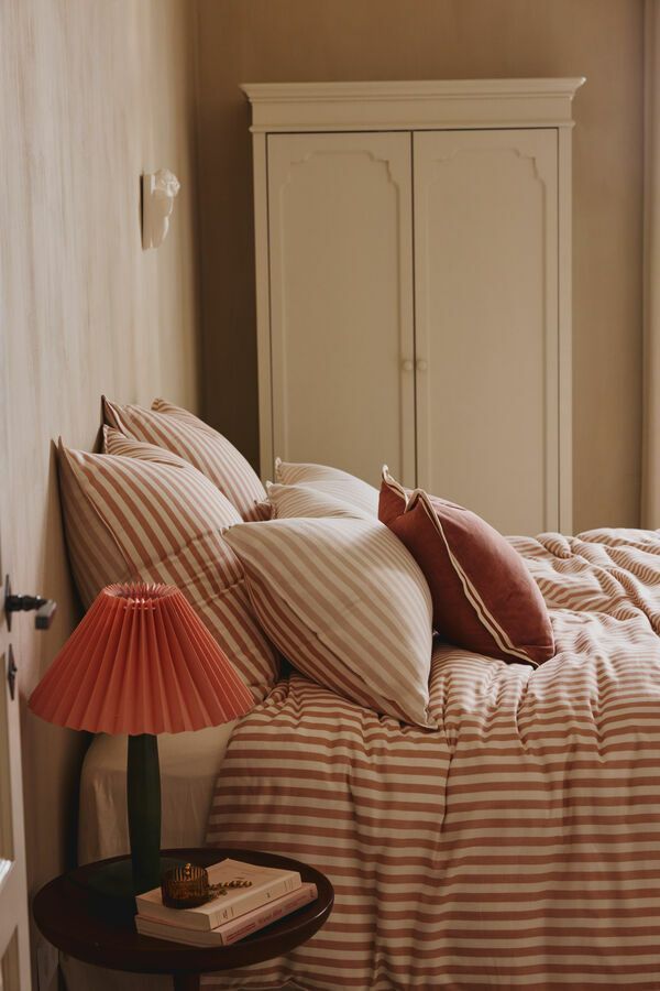 Chambre avec linge de lit à rayures, oreillers, lampe et armoire blanche.