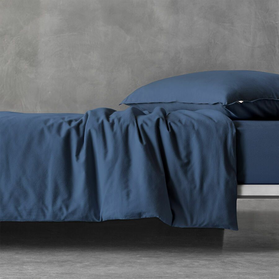 Une housse de couette bleu foncé et un oreiller assorti sur un lit adossé à un mur en béton gris texturé.