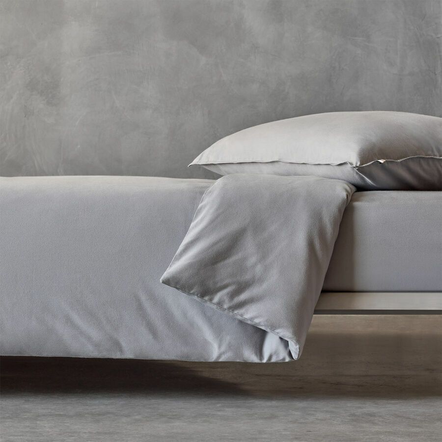 Gros plan sur une housse de couette gris clair et un oreiller sur un lit adossé à un mur gris texturé.