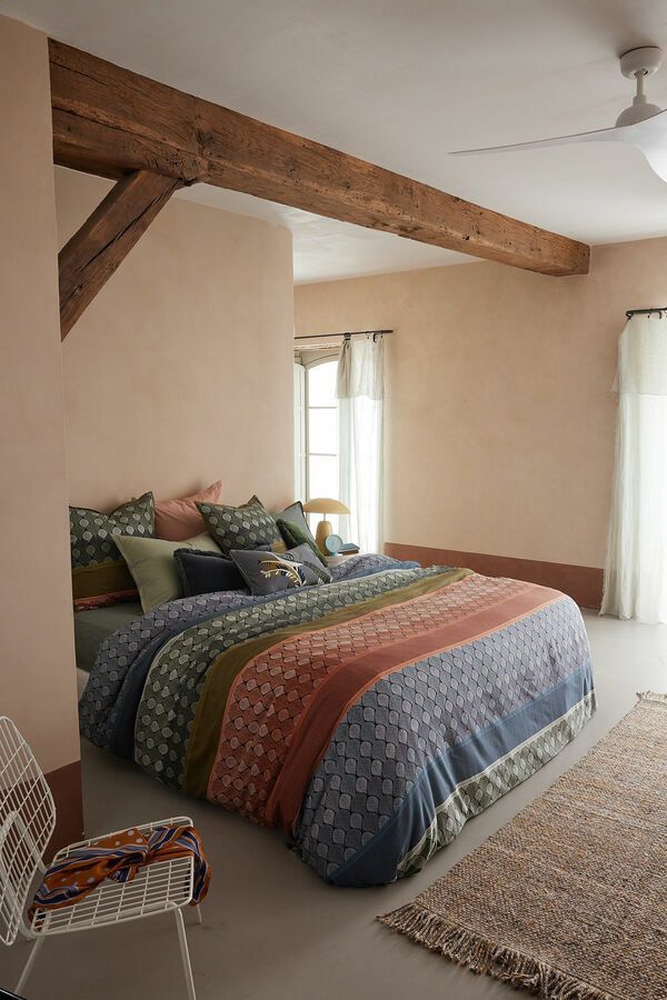 Une chambre avec un lit, une chaise, un tapis et un ventilateur de plafond.