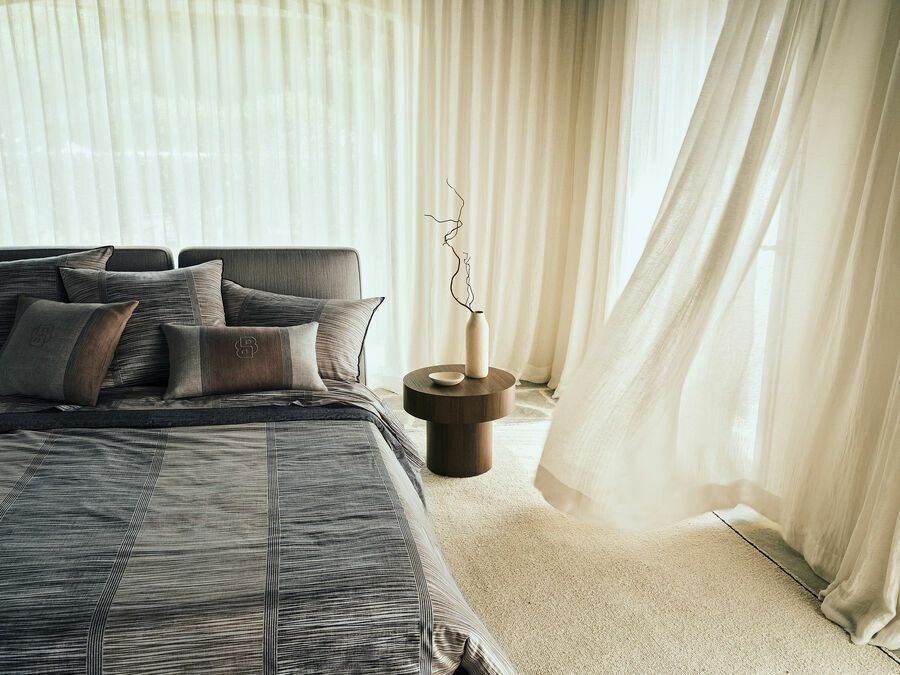 Une chambre avec un lit, une table de chevet et une fenêtre avec des rideaux flottant au vent.