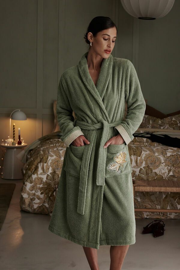 Une femme vêtue d'une robe verte se tient dans une chambre à côté d'un lit.