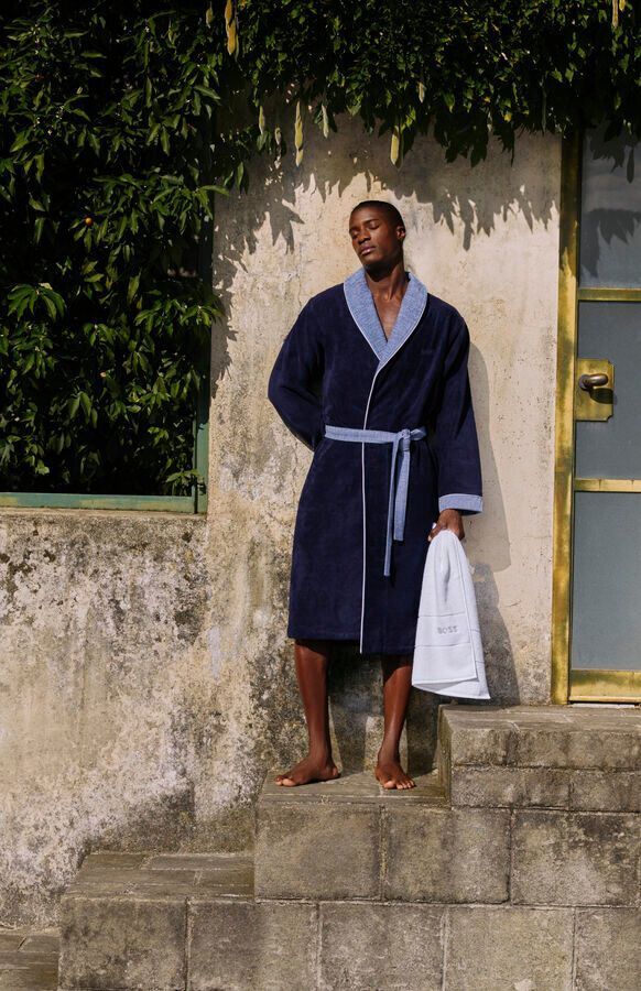 Un homme en peignoir se tient sur des marches tenant une serviette.