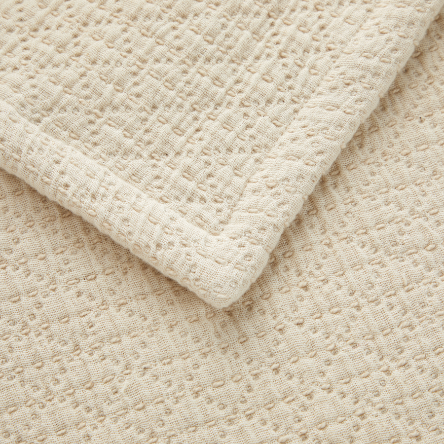 Gros plan sur un tissu plié, de couleur crème, à motif gaufré texturé et ourlet cousu.