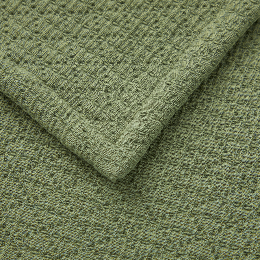 Gros plan sur un textile vert sauge à motif texturé en gaufre et ourlet cousu.