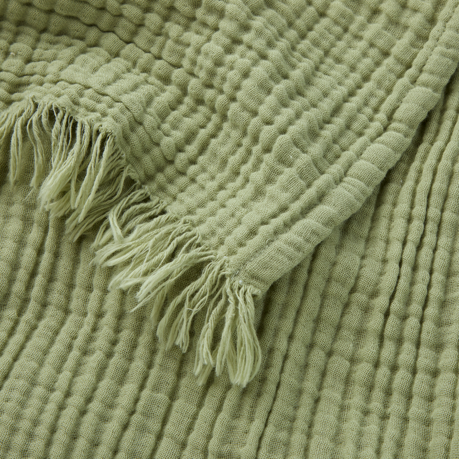 Une couverture en coton vert sauge clair, à motif gaufré texturé et bords frangés.