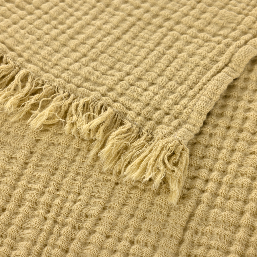 Gros plan sur un plaid beige texturé à tissage gaufré avec des bords effilochés.