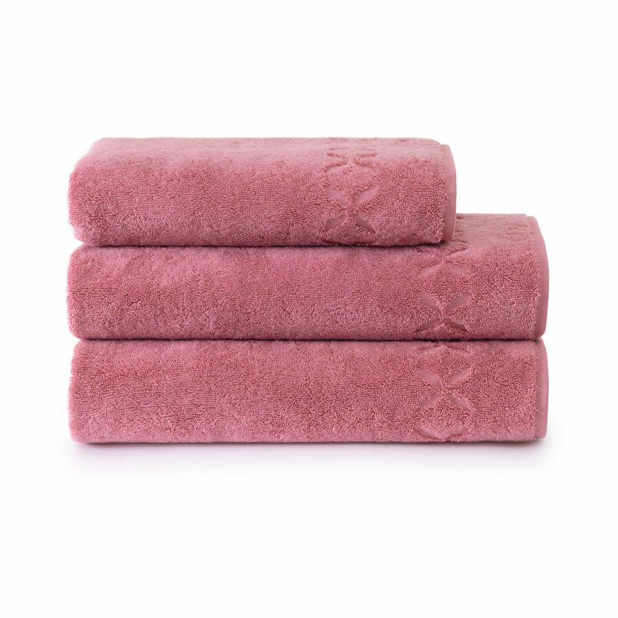 Pile de trois serviettes de bain rose poudré à motifs floraux en relief.