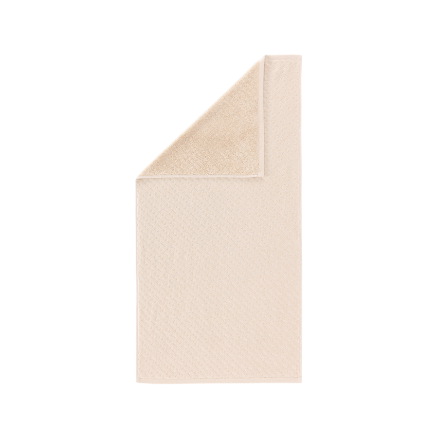 Une serviette de toilette beige clair à motif texturé, présentée pliée dans le coin supérieur pour révéler un dessous plus doux.