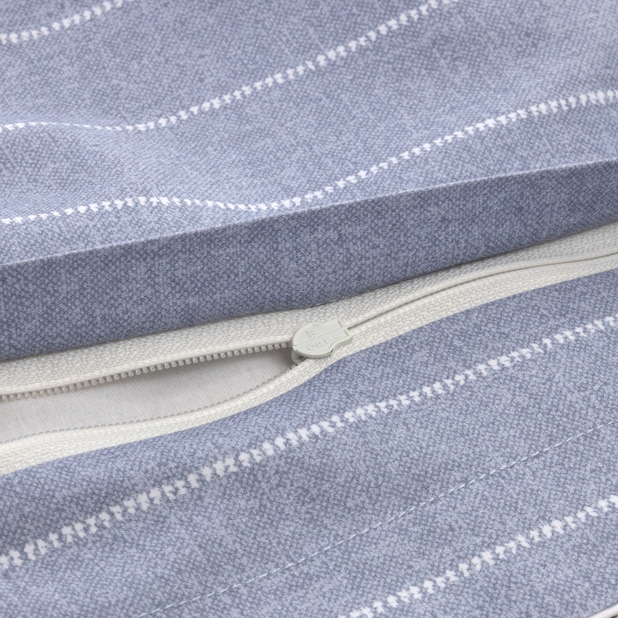 Gros plan sur une housse de coussin texturée bleu clair à fines rayures blanches, avec une fermeture éclair beige ouverte.
