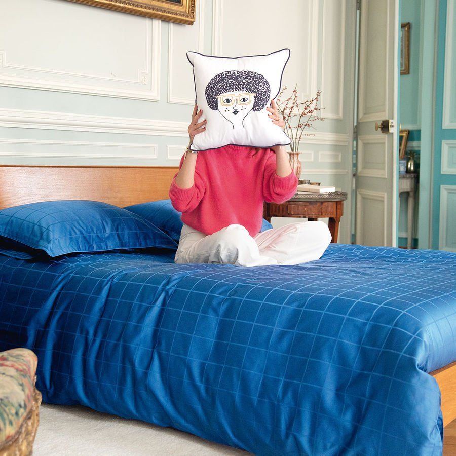 Une femme assise sur un lit se couvrant le visage avec un oreiller