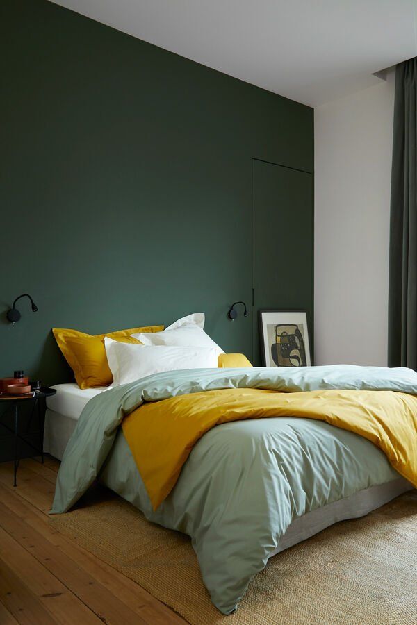 Une chambre avec un mur vert et un lit avec une couette jaune.