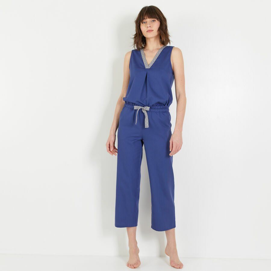 Une femme en combinaison bleue se tient devant un mur blanc