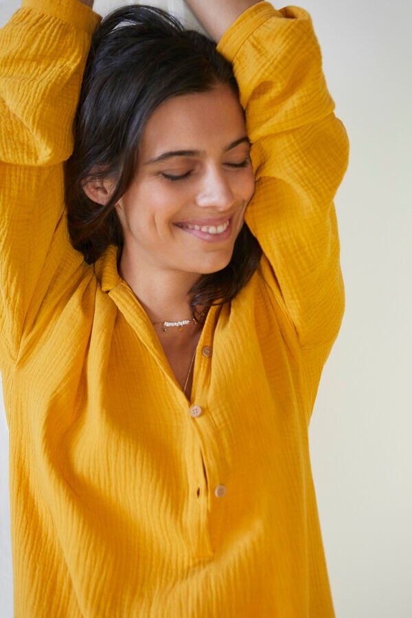 Une femme en chemise jaune sourit avec les bras en l'air.