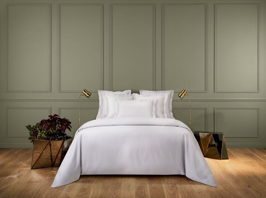 Un lit avec des draps et des oreillers blancs dans une chambre aux murs verts.