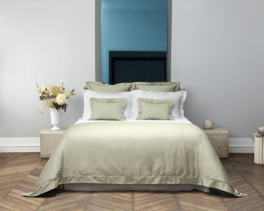 Un lit avec une couette blanche et des oreillers dans une chambre avec un miroir.