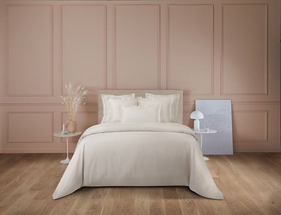 Un lit avec une couette et des oreillers blancs dans une chambre aux murs roses.