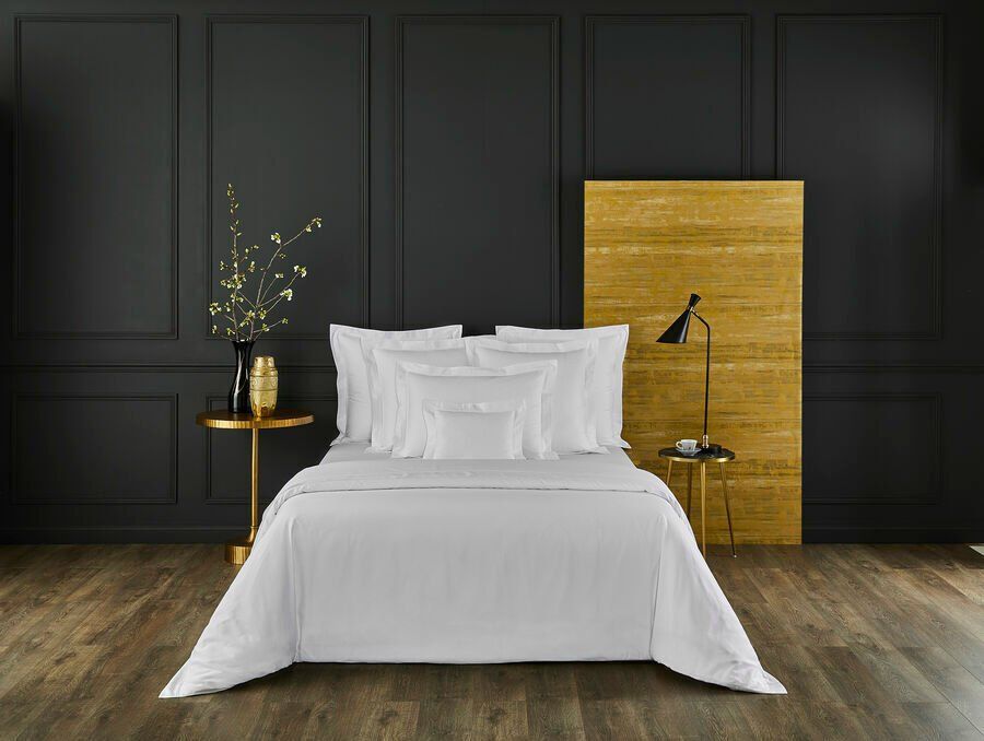 Un lit avec des draps et des oreillers blancs dans une chambre aux murs noirs.