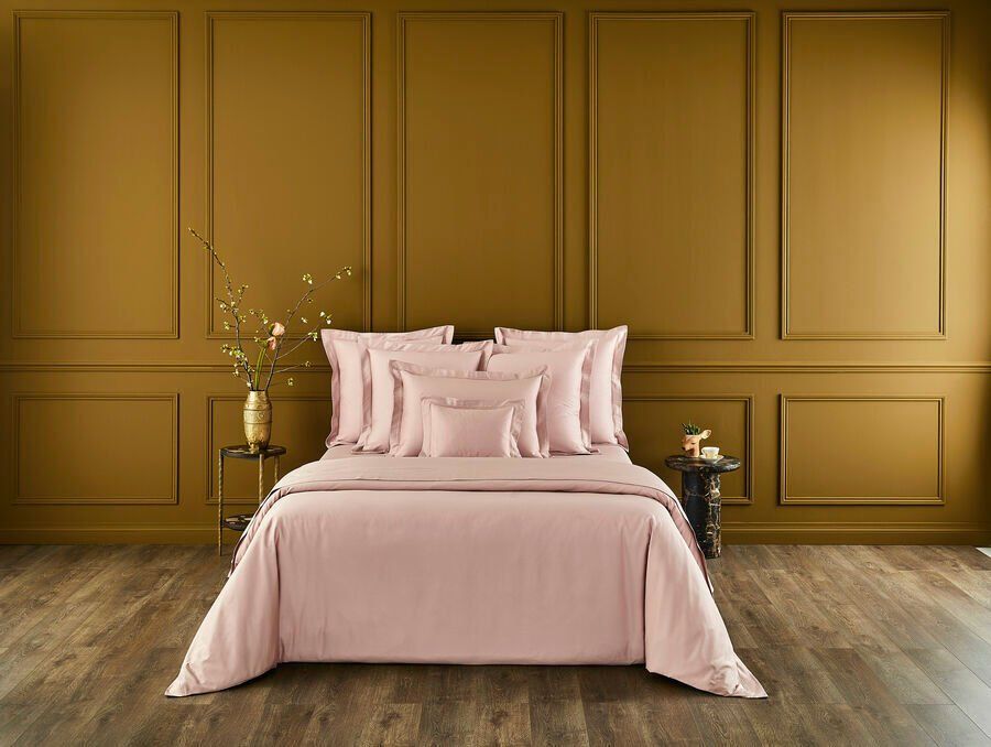 Un lit avec une couette et des oreillers roses dans une chambre.