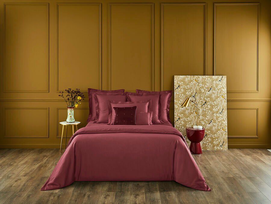 Un lit avec une couette et des oreillers violets dans une chambre avec un plancher en bois.