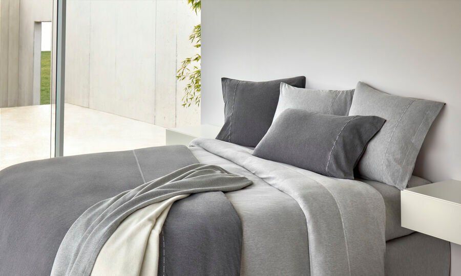 Un lit avec des draps et des oreillers gris dans une chambre