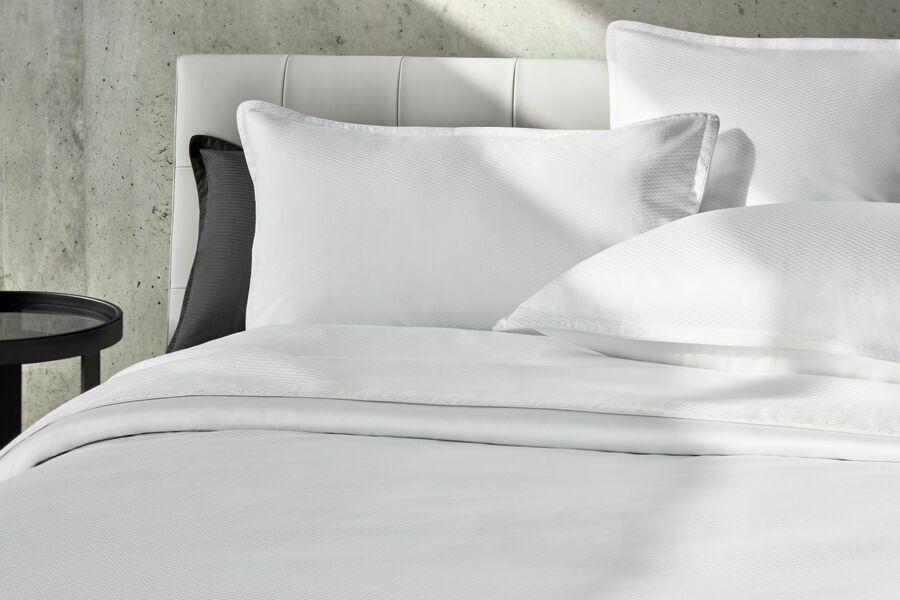 Un lit avec des draps blancs et des oreillers à côté d'une table.