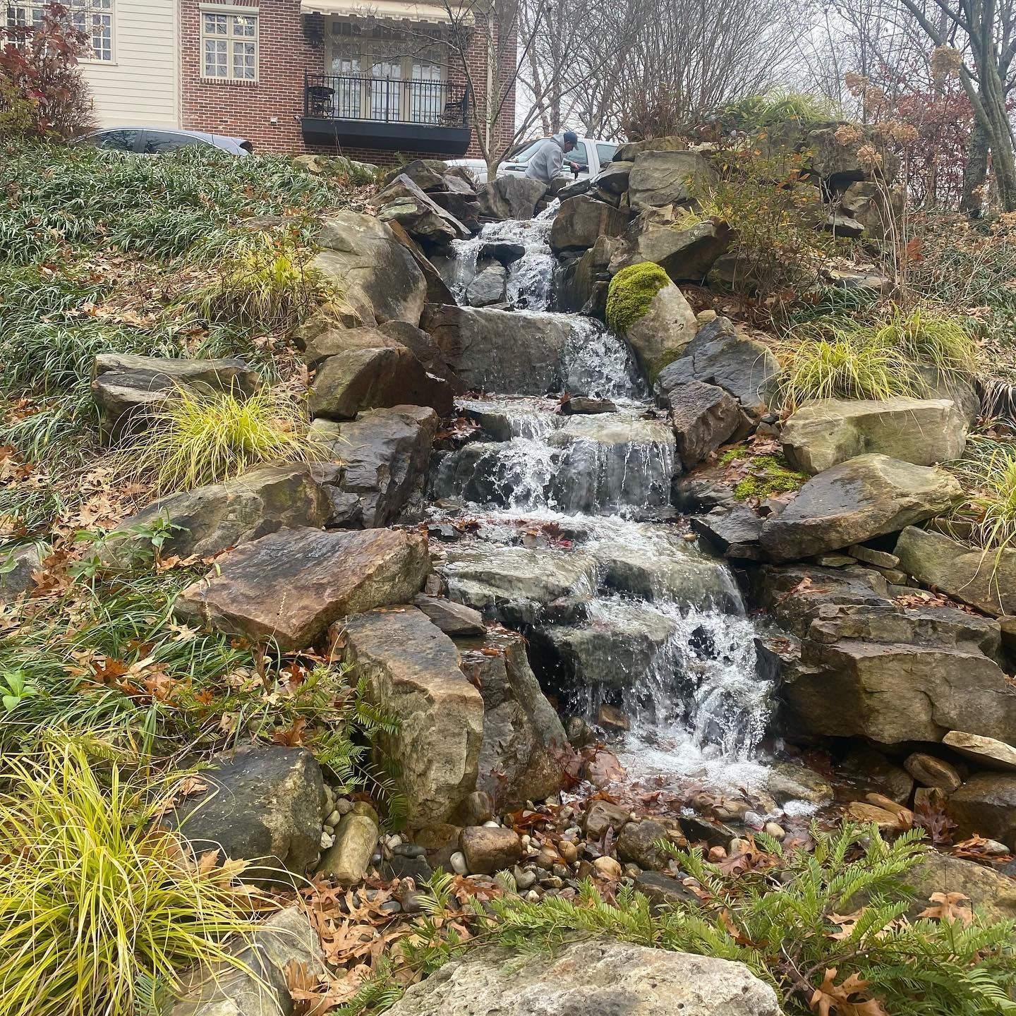 A small waterfall is surrounded by rocks and plants in a garden.