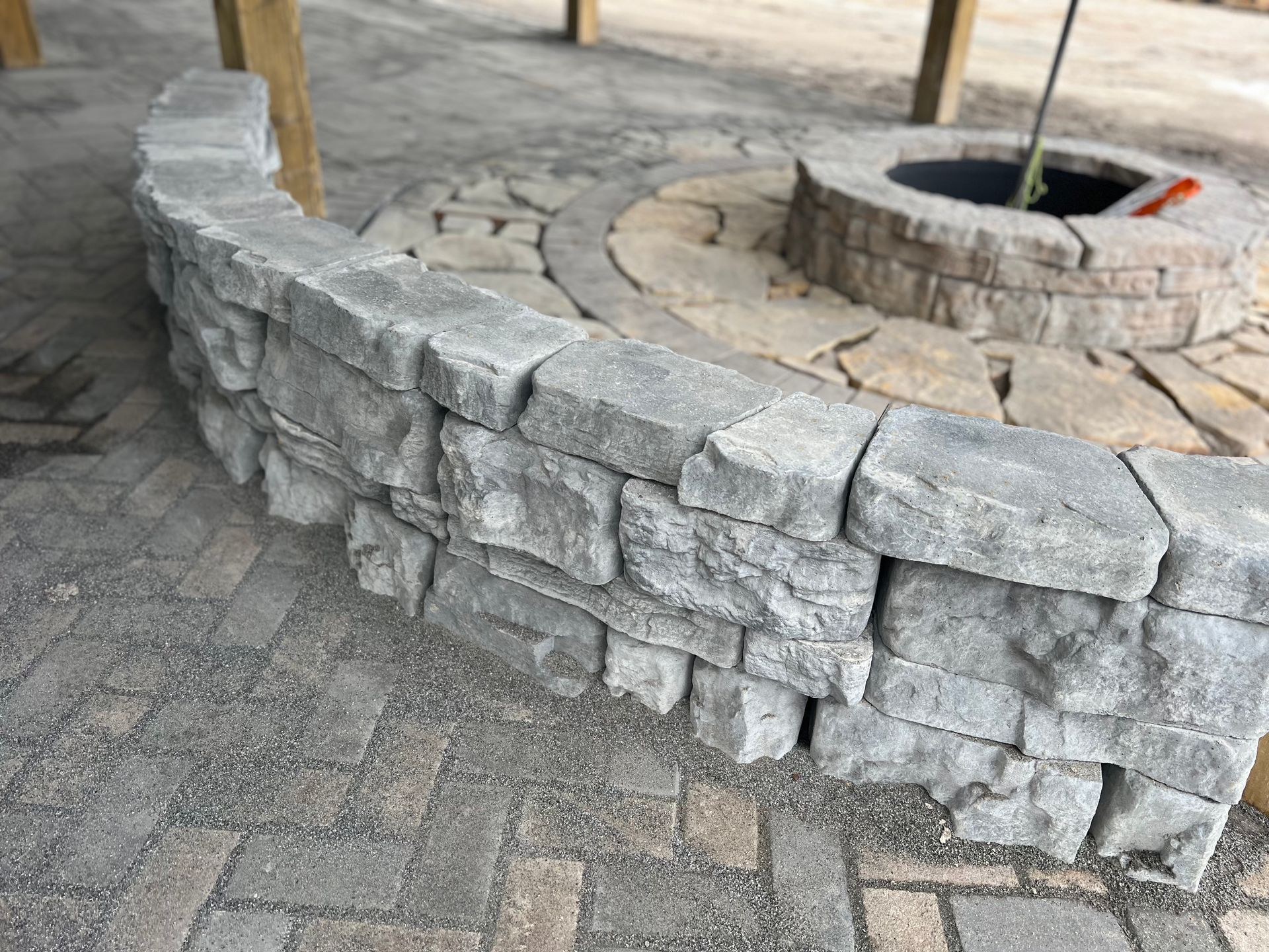 A fire pit is surrounded by a stone wall on a brick patio.