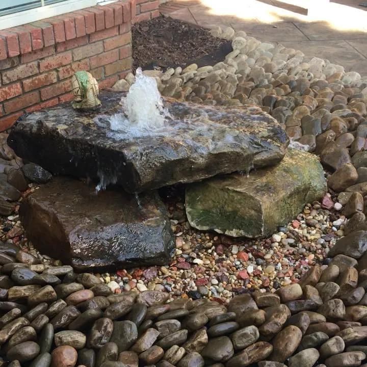 A water fountain is surrounded by rocks and a brick wall