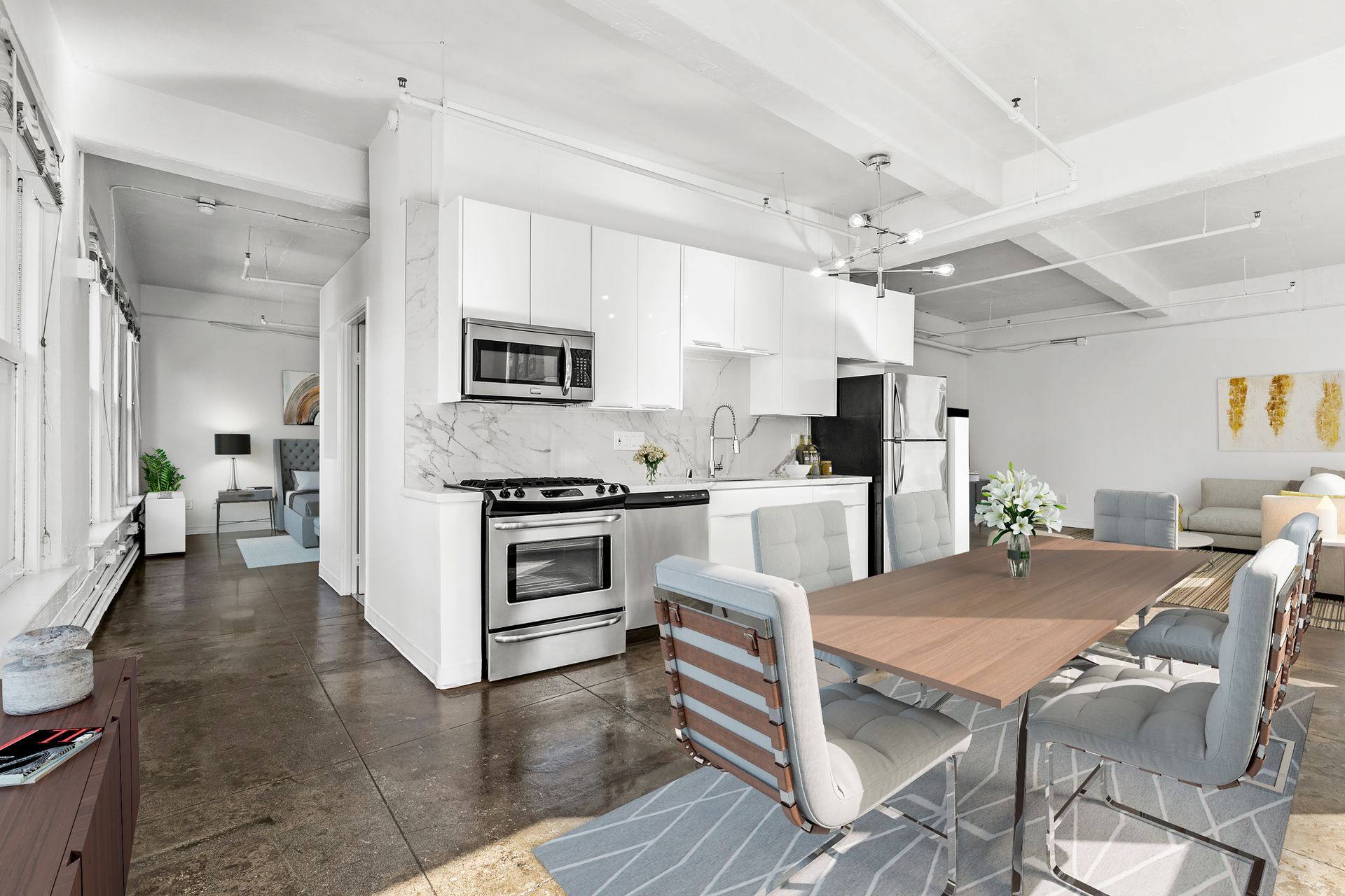 Bright open-plan kitchen and dining area with white cabinets, wood table, and gray chairs
