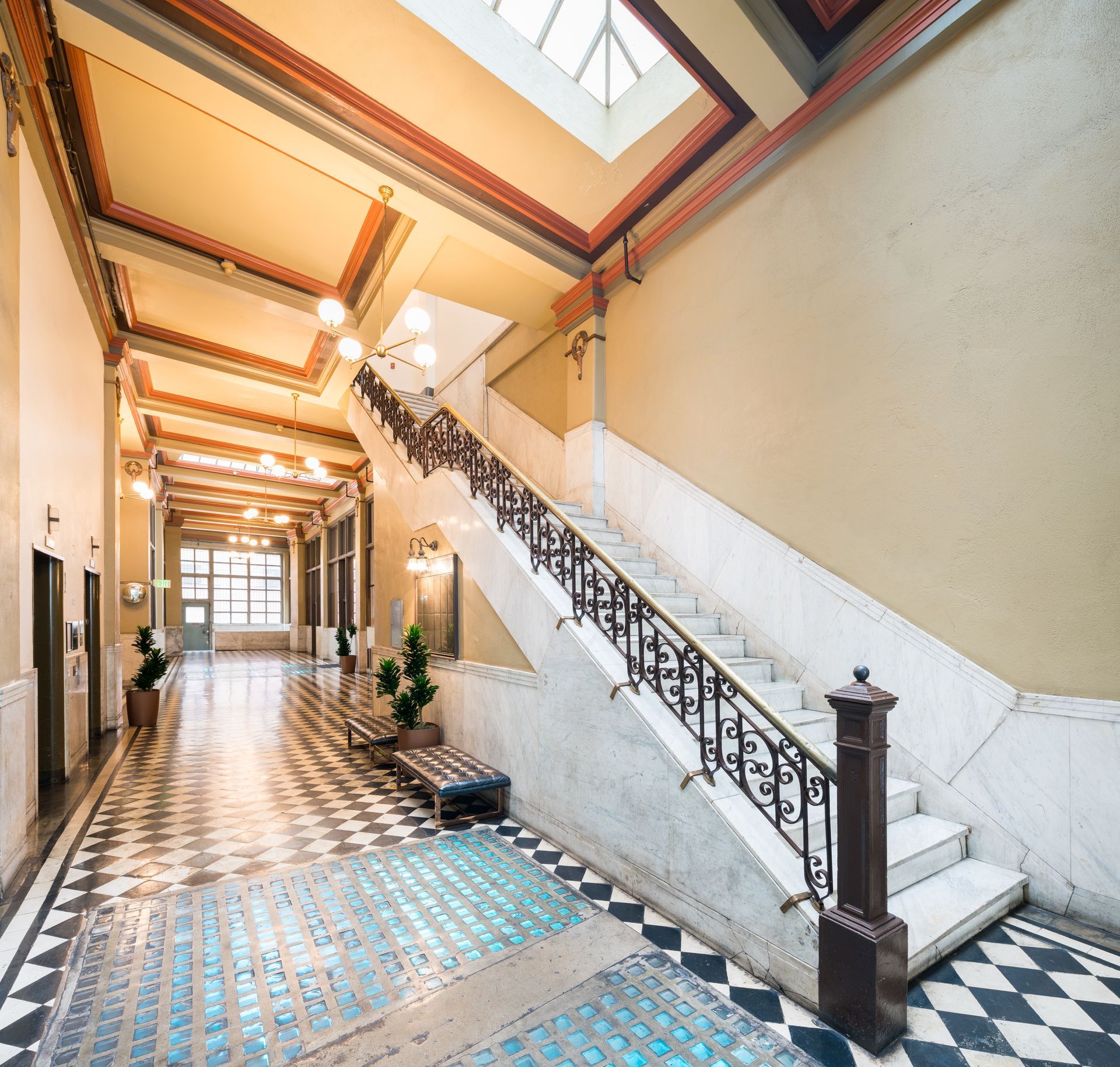 Bright indoor hallway with patterned tile floor, staircase, and skylight ceiling in an old building