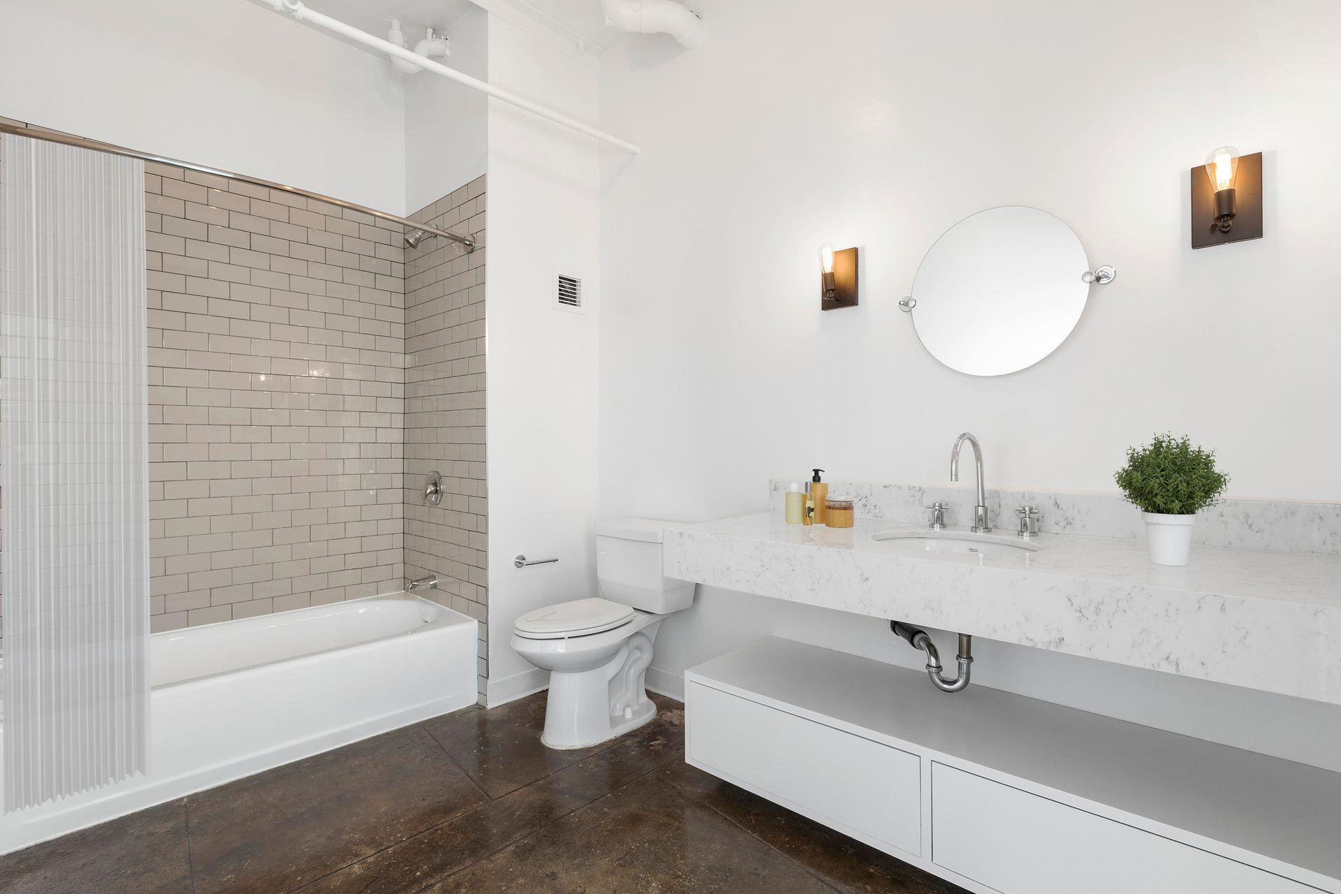 Bright modern bathroom with white vanity, round mirror, toilet, tub, and tiled shower