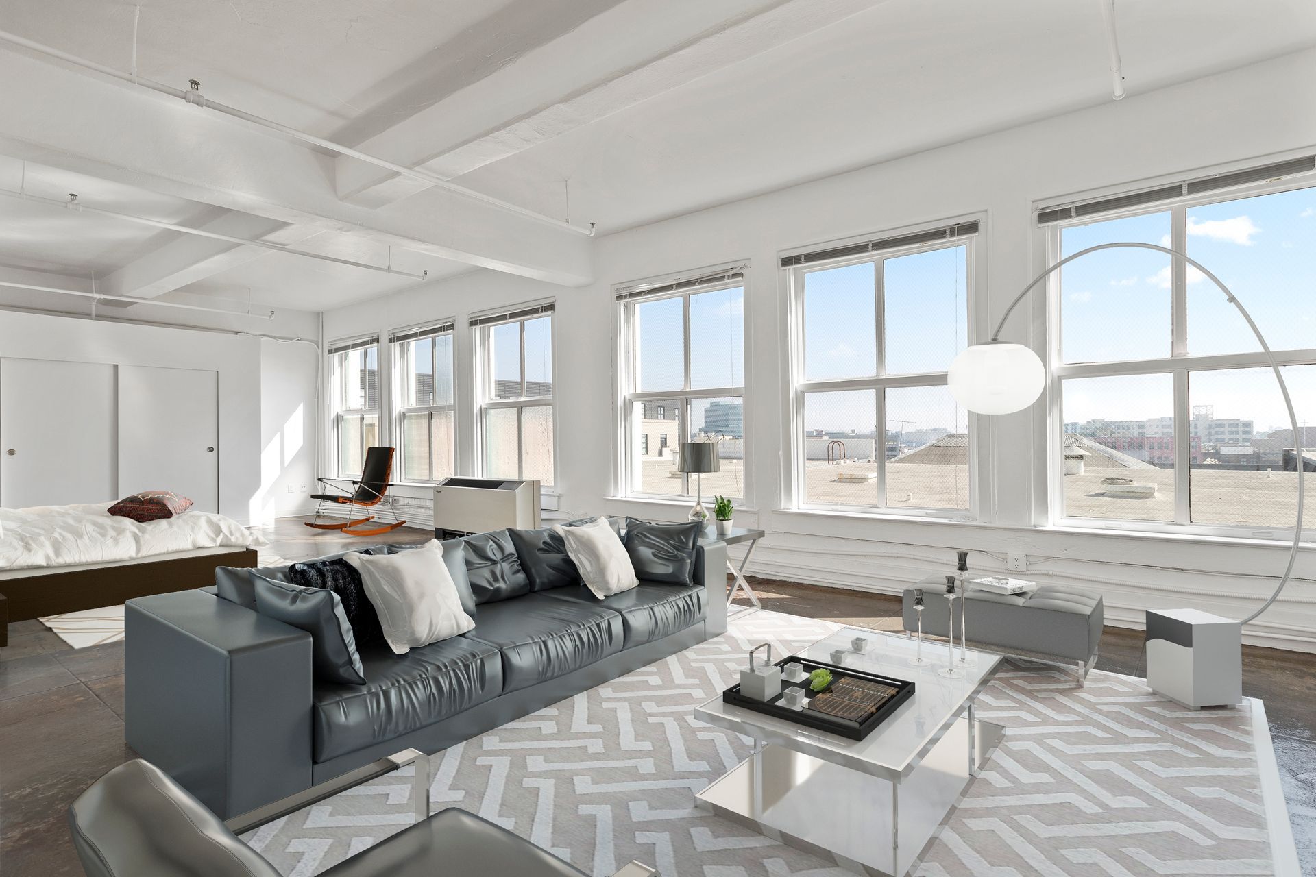 Bright modern living room with a gray sofa, white coffee table, and large windows overlooking water.