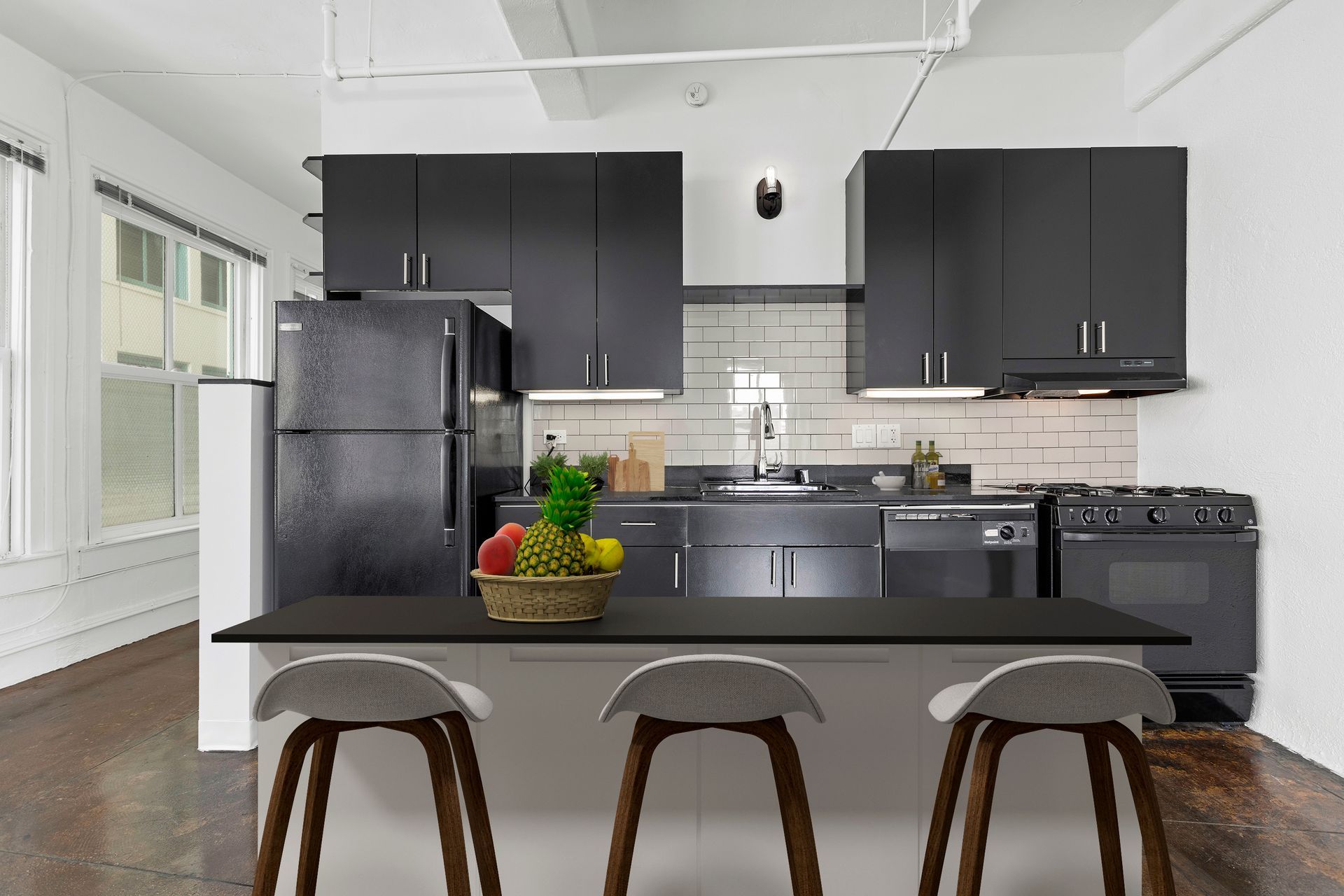 Modern black-and-white kitchen with island, three stools, and bowl of fruit