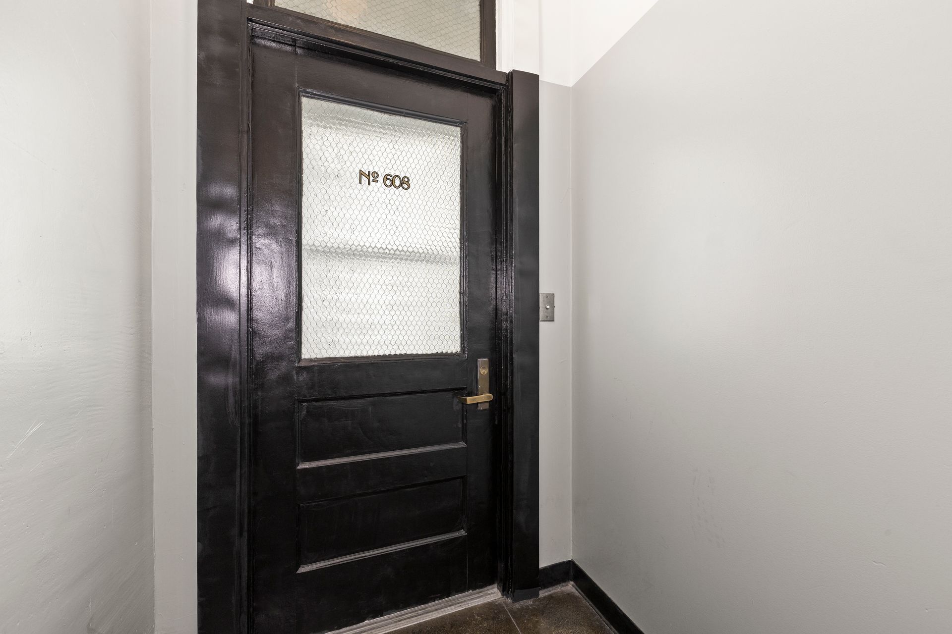 Black door with frosted glass window in a narrow hallway